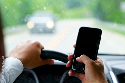 Don't text and drive ! A man is texting with a finger while a car is arriving in front.  focus on the finger, focus on telephone, focus on the car coming.
