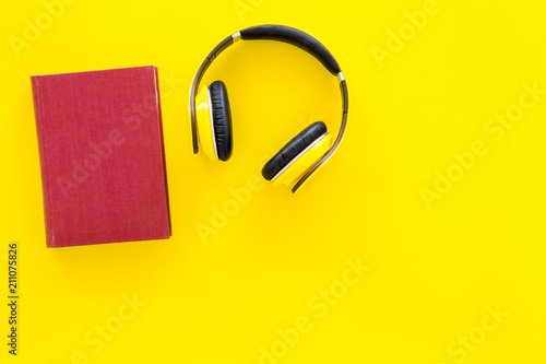 Distance education, e-learning concept. Headphones near hardback book with empty cover on yellow background top view copy space