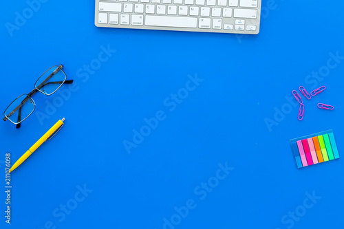Education concept. Stationery frame with glasses and keyboard on blue background top view copy space