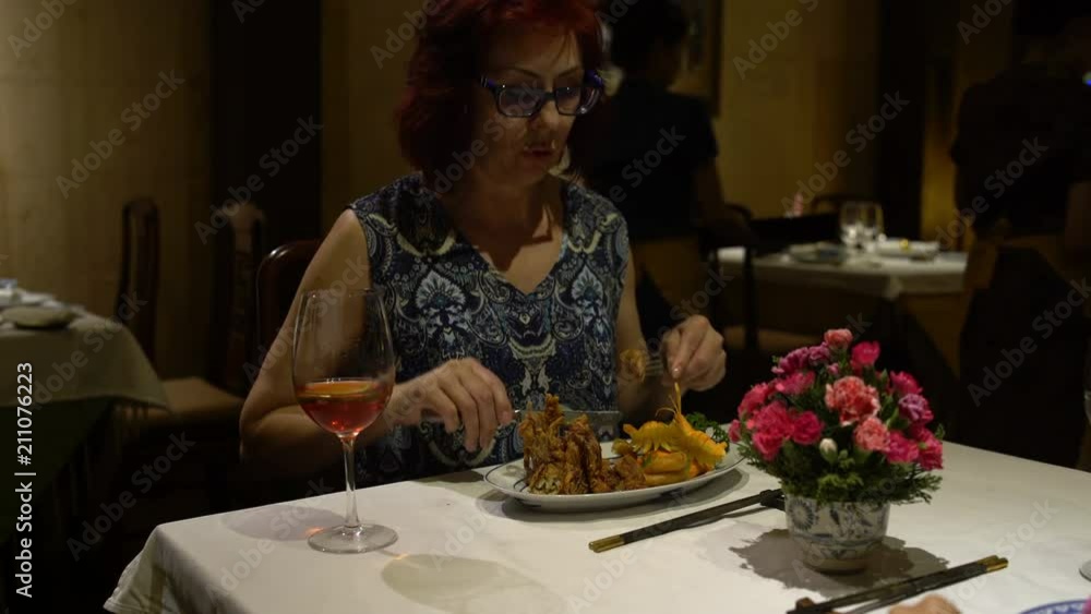 Woman sitting at the table eating the dish in the form of a Lotus Flower and drinking red wine Woman sitting at the table eating the dish in the form of a Lotus Flower and drinking red wine