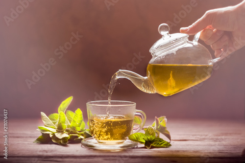  A woman's hand pours herbal tea from a glass teapot into a cup. The concept of a healthy diet.