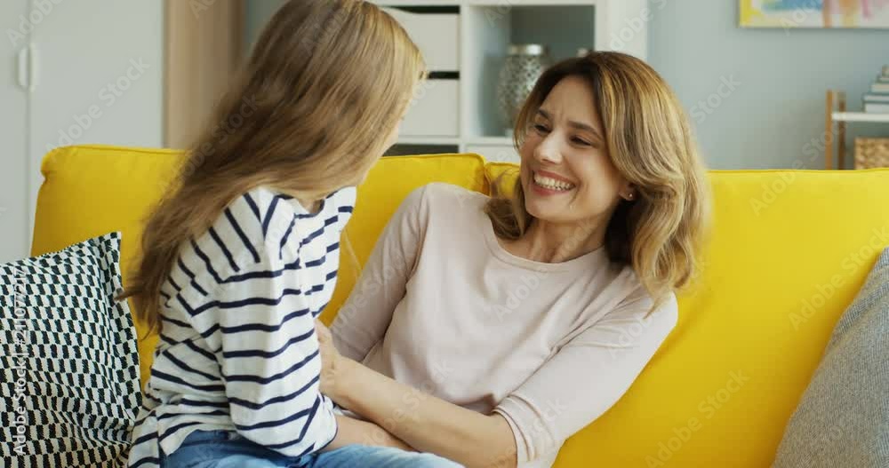 Caucasian beautiful mother and teenager daughter having fun on the yellow sofa and tickling in the living room. Indoors. Caucasian beautiful mother and teenager daughter having fun on the yellow sofa and tickling in the living room. Indoors.