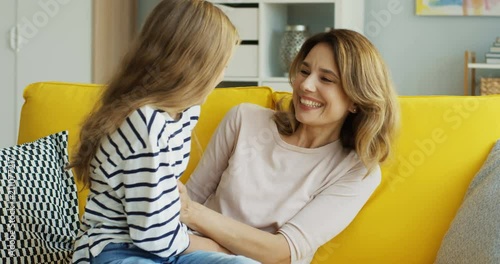 Caucasian beautiful mother and teenager daughter having fun on the yellow sofa and tickling in the living room. Indoors. photo