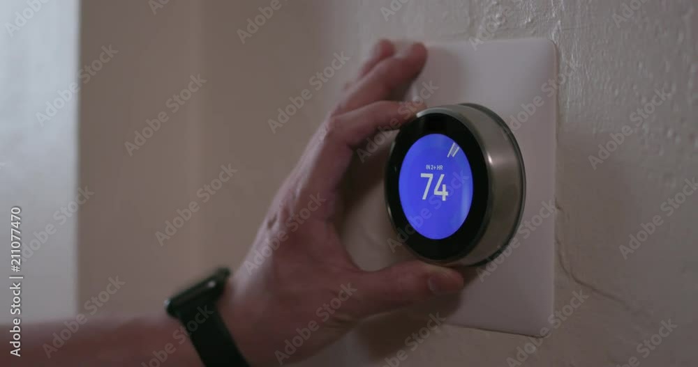 Man Adjusting Smart Thermostat Gadget At Home with Smart Watch - Medium Man Adjusting Smart Thermostat Gadget At Home with Smart Watch - Medium