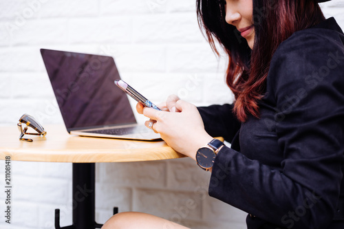 Young fashionable Asian business woman using a mobile phone and laptop over white brick background