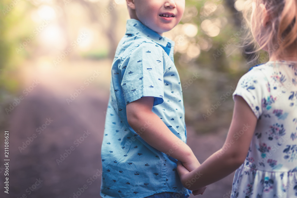 Happy kids walking outdoor at park hold their hands.