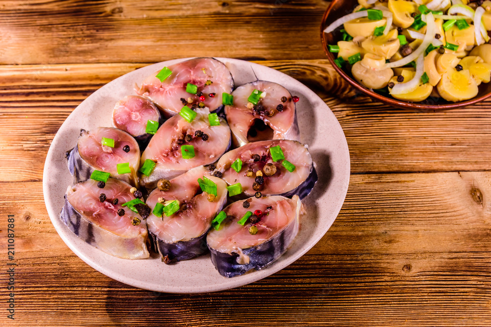 Sliced scomber fish and canned mushrooms with green onion on a ceramic plates on wooden table