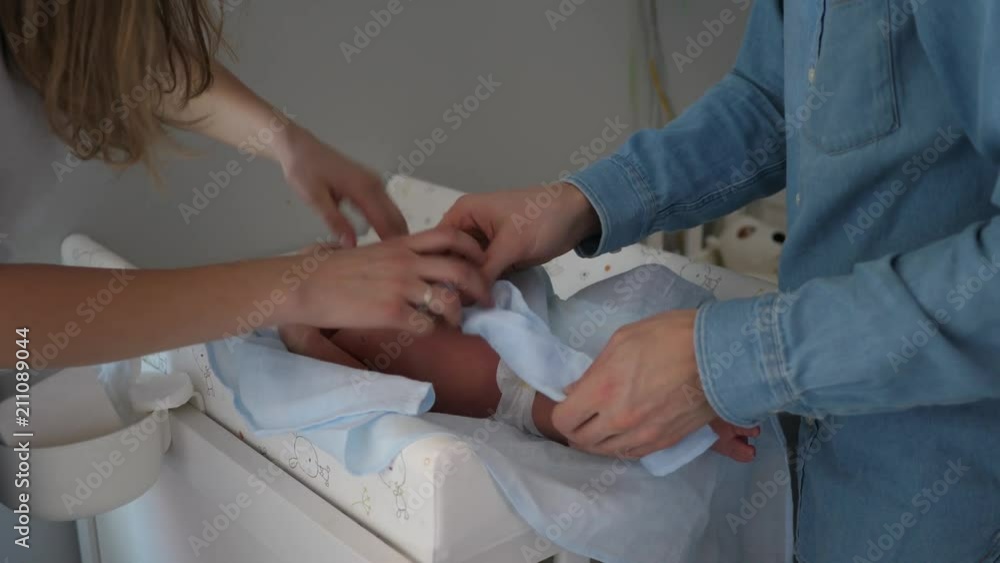 New parents young couple mother and father learn to swaddle newborn baby in nappy at home New parents young couple mother and father learn to swaddle newborn baby in nappy at home