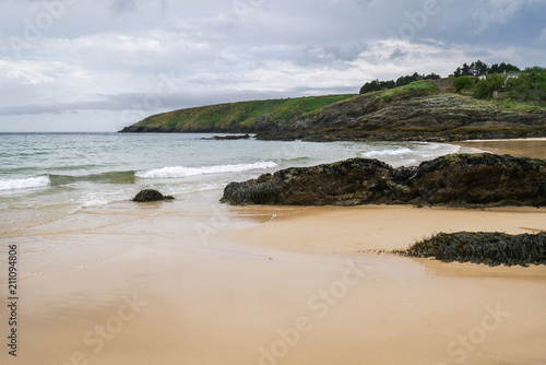 Typical brittany landscape with lonely beach with rocks covered with algae and seaweed and cloudy sky in the background