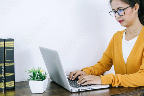 Happy casual young asian woman working in home or small office with using a laptop and document report on desk as a freelancer