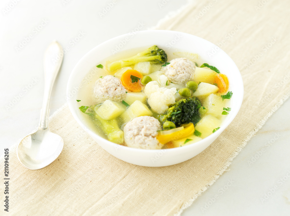 bowl of soup, a cup of broth and vegetables, meatballs made of turkey and chicken, side view bowl of soup, a cup of broth and vegetables, meatballs made of turkey and chicken, side view