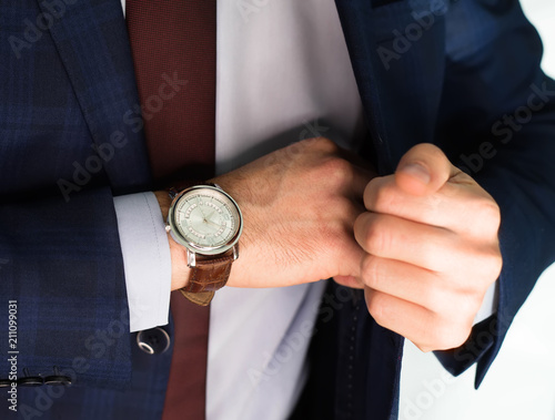 Closeup fashion image of luxury watch on wrist of man.body detail of a business man.Man's hand in pocket closeup at white background.Man wearing blue jacket and white shirt and tie.