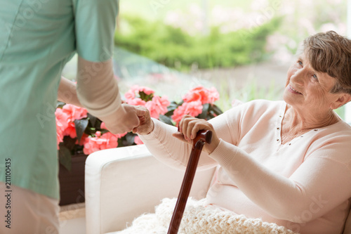 Doctor helping an elderly woman with Parkinson's disease get up from a sofa in a rehabilitation facility