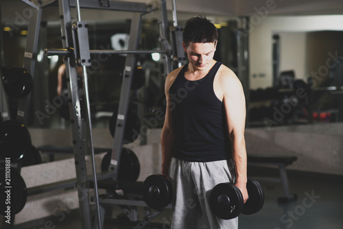 Young and strong man using dumbbells at the gym. Toned image