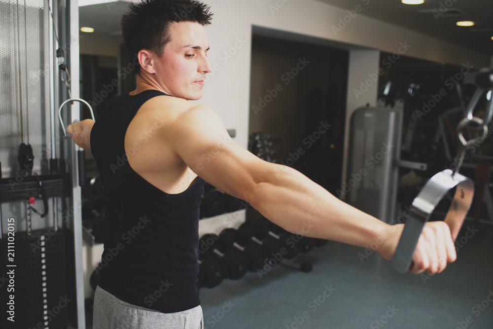 Young strong man doing exercises on the simulator at the gym. Toned image Young strong man doing exercises on the simulator at the gym. Toned image