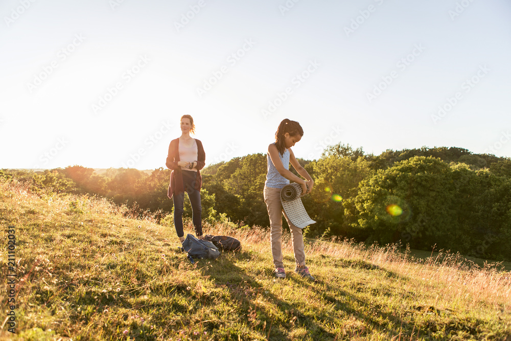 Full length of girl rolling mat while standing by mother on field against sky during sunset Full length of girl rolling mat while standing by mother on field against sky during sunset