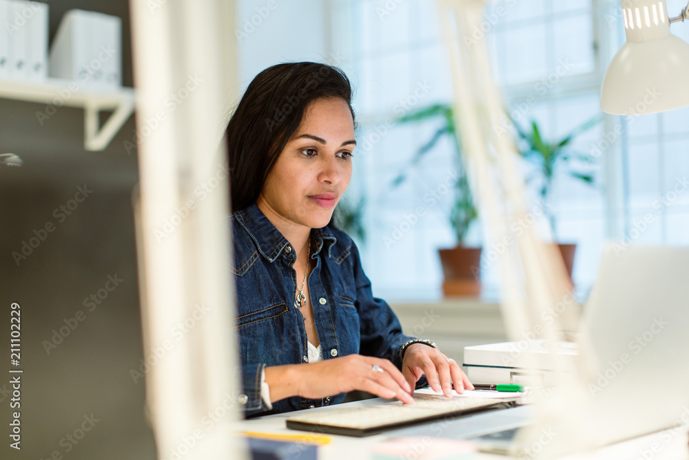 Confident businesswoman using laptop while sitting at desk in creative office Confident businesswoman using laptop while sitting at desk in creative office