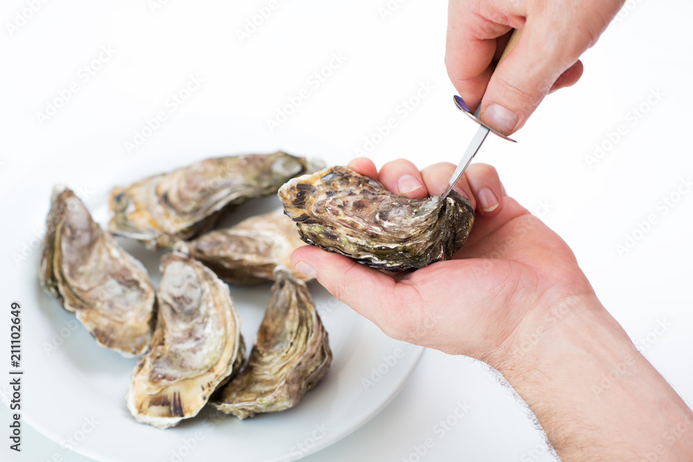 Fresh oyster. Man open fresh oyster. Raw fresh oyster is on white round plate, image isolated, with soft focus. Restaurant delicacy. Saltwater oyster. Fresh oyster. Man open fresh oyster. Raw fresh oyster is on white round plate, image isolated, with soft focus. Restaurant delicacy. Saltwater oyster.