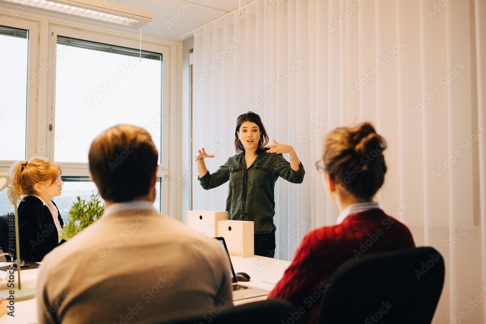 Confident businesswoman explaining strategy to colleagues sitting in board room at creative office Confident businesswoman explaining strategy to colleagues sitting in board room at creative office