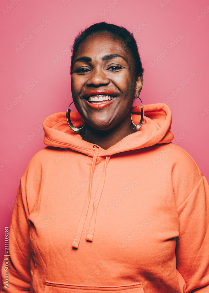 Portrait of smiling mid adult woman wearing orange hooded jacket over pink background Portrait of smiling mid adult woman wearing orange hooded jacket over pink background