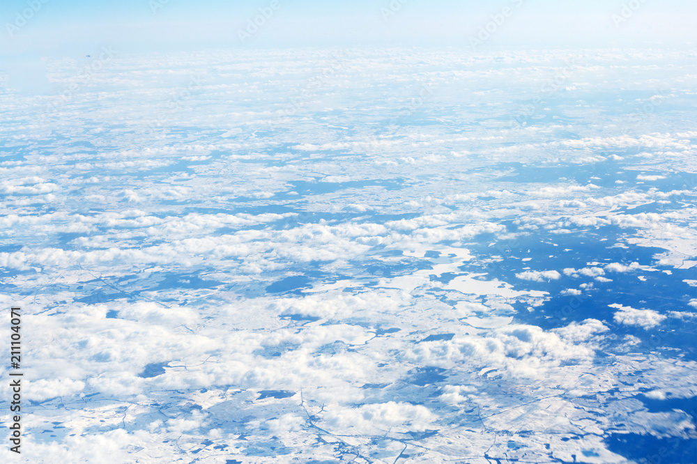 View from the top of the plane on clouds and snow-covered fields