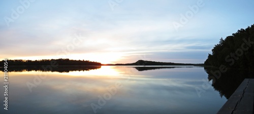 Fototapeta Naklejka Na Ścianę i Meble -  Sunset Over Beautiful Lake with Boat Silhouette and Cloudy Sky in background