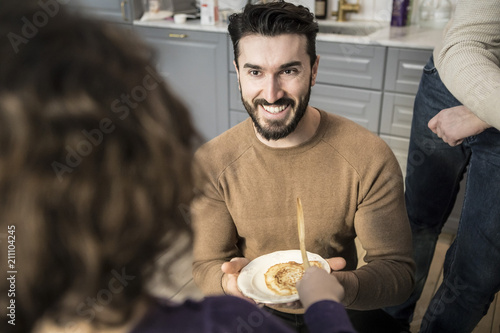 Smiling young father offering pancake to daughter in kitchen