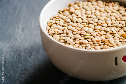 White ceramic bowl of green uncooked lentils isolated on black in perspective