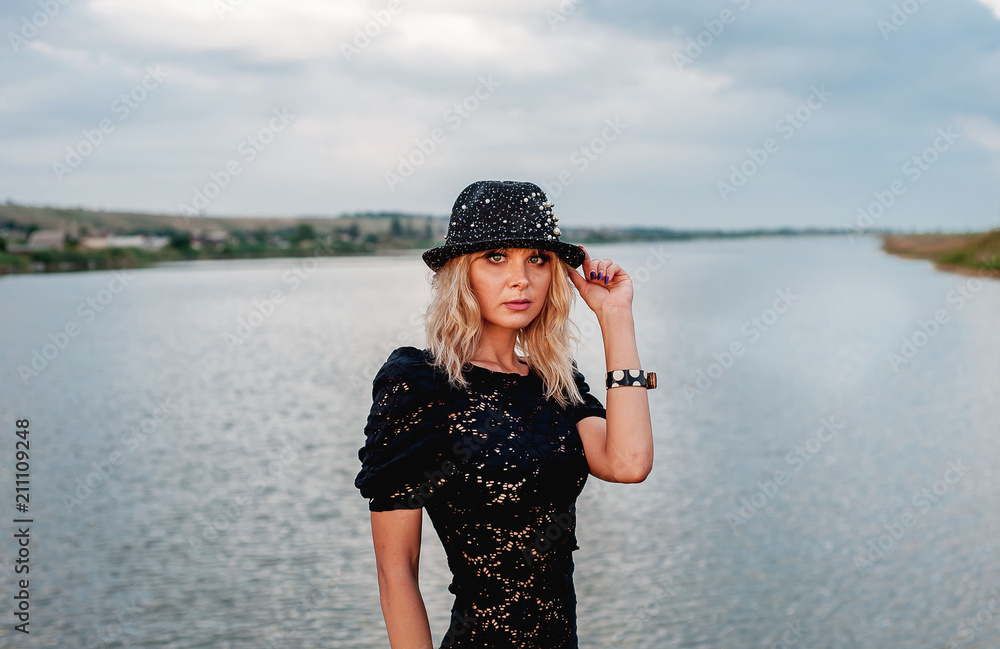 girl in black dress and hat in front of river