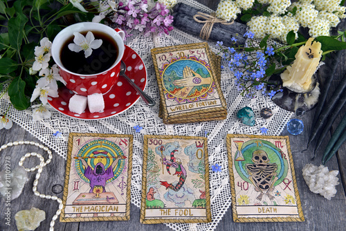 Tarot cards with cup of tea, flowers and black candles on planks. Occult, esoteric and divination still life. Halloween background with vintage objects and magic ritual