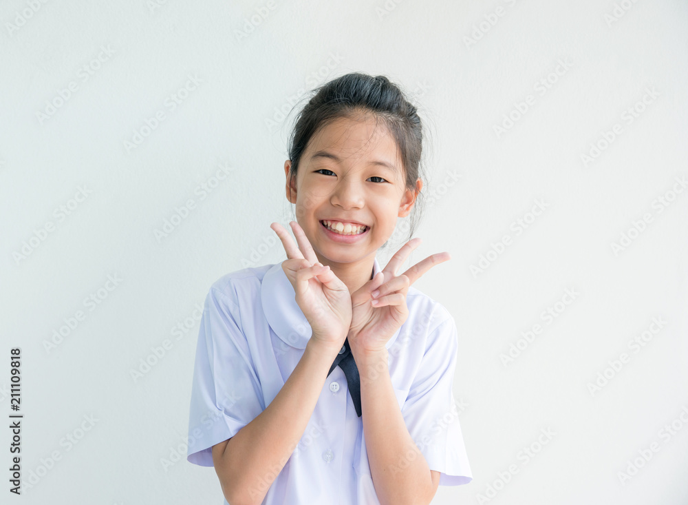 Happy little girl holding two finger gesture as sign as fighting with studying. Portrait of Smiling Thai primary school student in Thai uniform on white background and copy space. Education concept. Happy little girl holding two finger gesture as sign as fighting with studying. Portrait of Smiling Thai primary school student in Thai uniform on white background and copy space. Education concept.