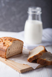 Banana bread in a pan with white parchment paper on a white wooden table with milk bottle in the background. Close up. Bakery concept