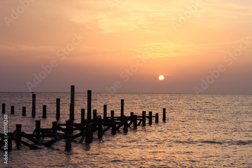 Sunrise on the sea. Wooden piles of destroyed pier sticking out of the water. The sun peeps out from behind the clouds. Red sea,Egypt. © Vera