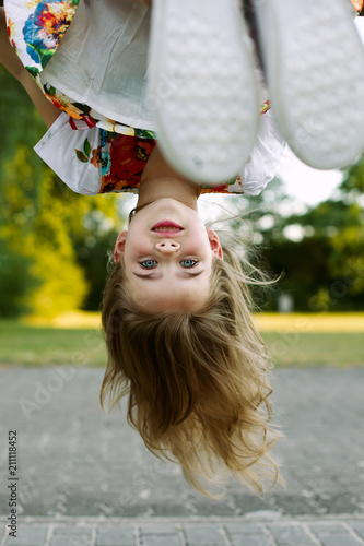 summer children's games and fun outdoors. Happy child girl hanging upside down on wooden Playground on Sunny day
