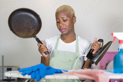 young beautiful sad and depressed afro American black woman with cooking pan and iron working stressed and tired at home kitchen overworked cleaning