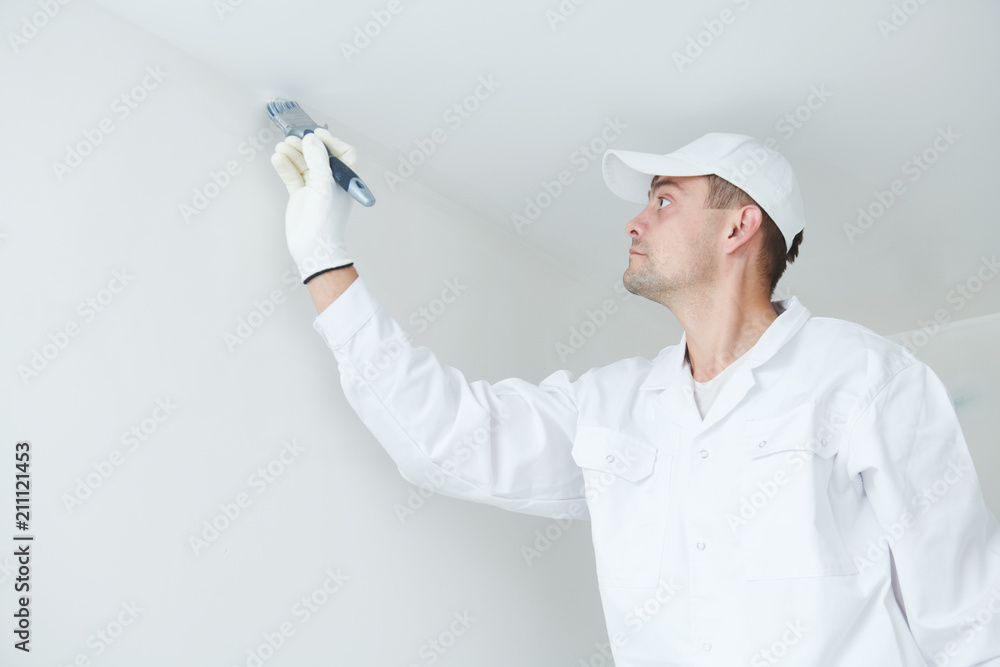 Painting. Painter with paint brush covering ceiling angle with white paint Painting. Painter with paint brush covering ceiling angle with white paint