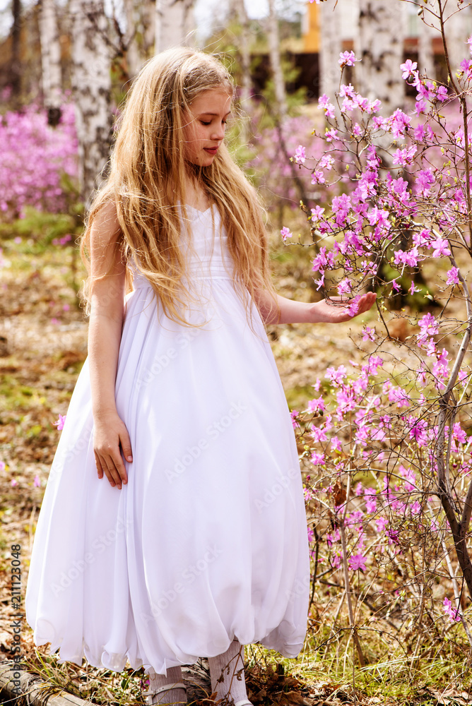 A child stands among the ledum and birch in white dress, smiling and fly hair A child stands among the ledum and birch in white dress, smiling and fly hair