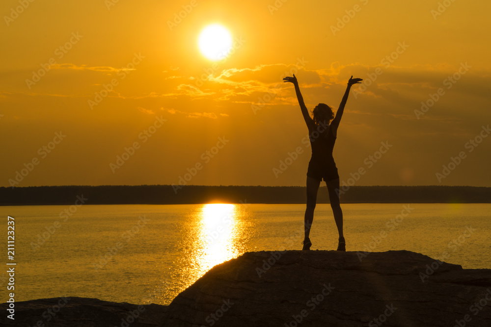 A young slender girl stands on top of a mountain holding her hands up towards the sun in the sunset. Walk in the open air. tourism, trekking, traveling. Success, joy.
