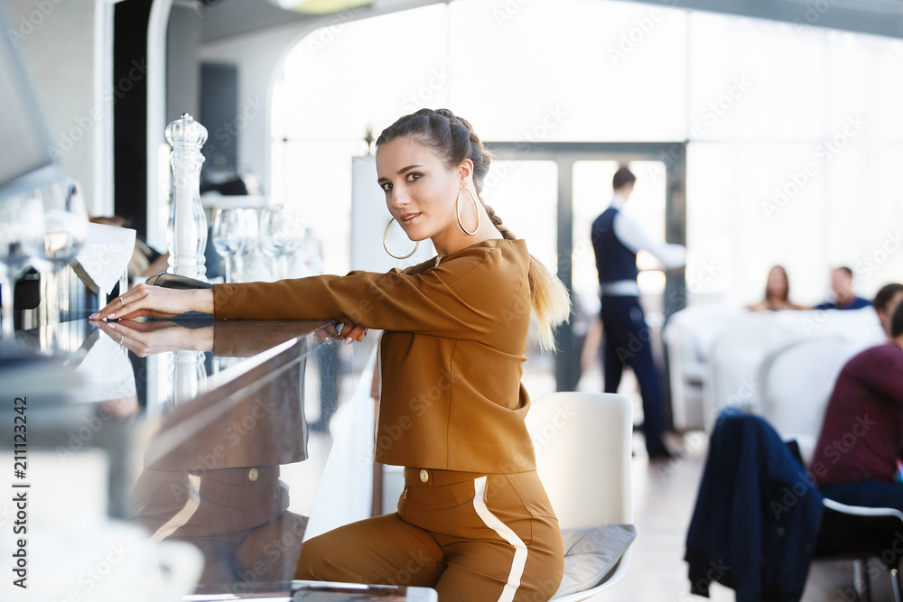 Obraz premium Fashion shot of young beautiful stylish woman sitting at a bar in luxury restaurant. Seductive attractive girl in expensive clothes at a party on a Friday night. City life, life style