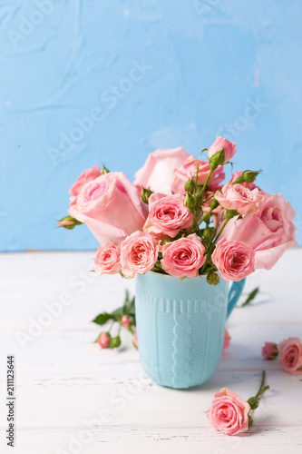 Pink roses flowers in blue cup against blue textured wall.