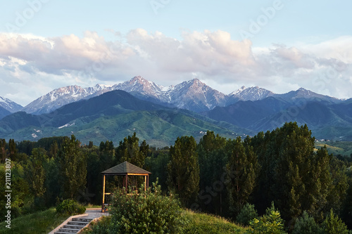 Summer houses with benches at evening with at snowy mountains background in dendra park of first president in Almaty, Kazakhstan.