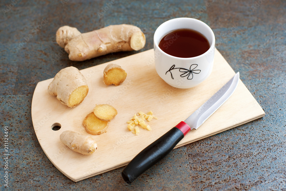 Tea with ginger. A cup of tea and sliced ginger root on a cutting board.