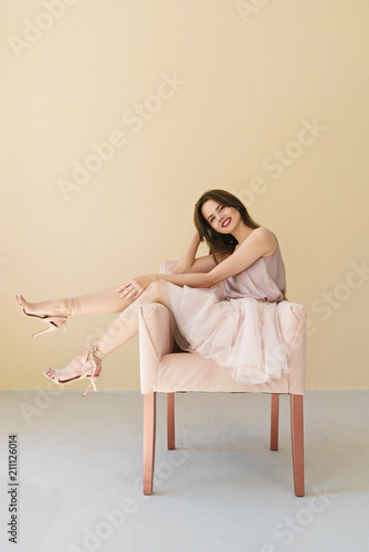 portrait of beautiful young woman sitting in a chair on beige background