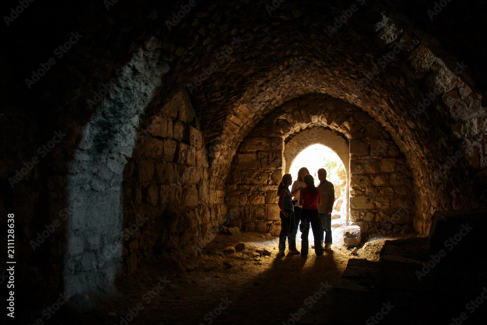 KERAK, JORDAN - Nov 2009: A small group of tourists stand in a dark chamber, silhouetted by glowing sunlight through an archway window inside the ancient crusader castle at Karak near Amman in Jordan