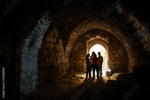 KERAK  JORDAN - Nov 2009  A small group of tourists stand in a dark chamber  silhouetted by glowing sunlight through an archway window inside the ancient crusader castle at Karak near Amman in Jordan