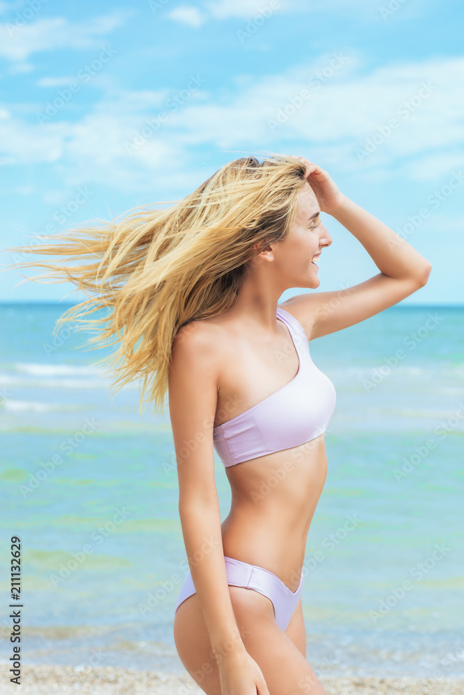 A beautiful young girl with light hair in a light swimsuit relax on beach  in the sea in sunny hot day Stock Photo | Adobe Stock