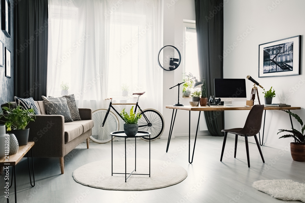 Bright living room interior with sofa with cushions, bike under the window with curtains and hairpin desk with lamp and computer for remote work Bright living room interior with sofa with cushions, bike under the window with curtains and hairpin desk with lamp and computer for remote work
