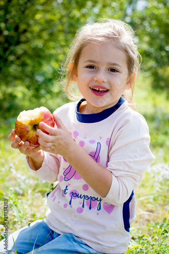 baby girl eating red apple in summer