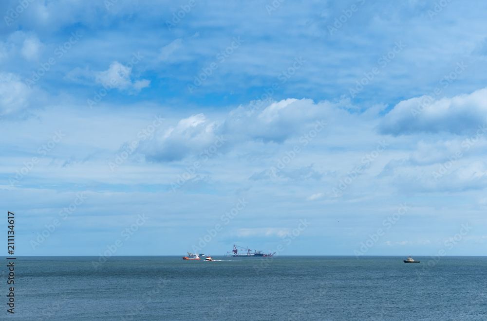 Ships in the sea on the horizon. Oil drilling in the sea. Calm and cloudy sky.