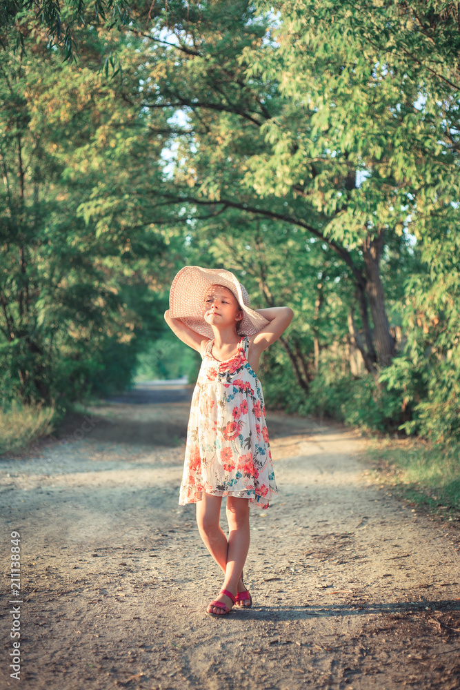 A beautiful school girl in a pink hat in the rays of the sunset on a summer evening on nature.